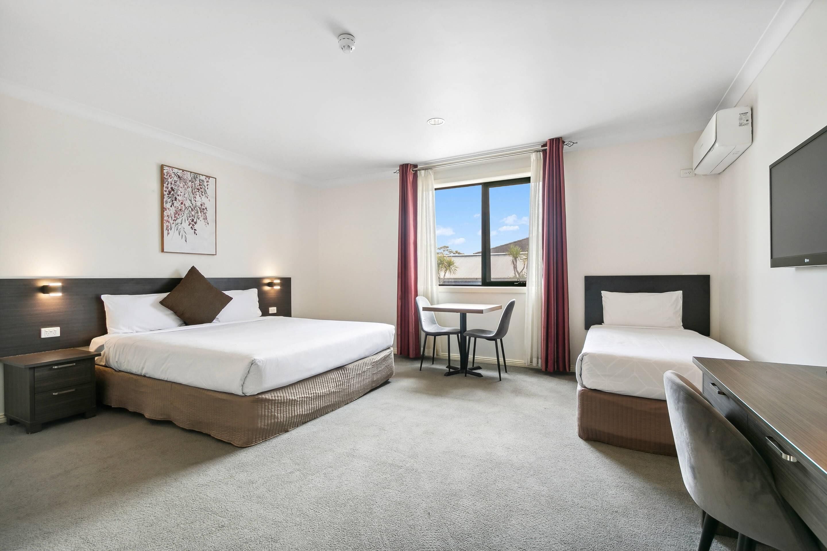 A hotel room with a large bed, a desk, a chair, a small table, and a window with curtains.