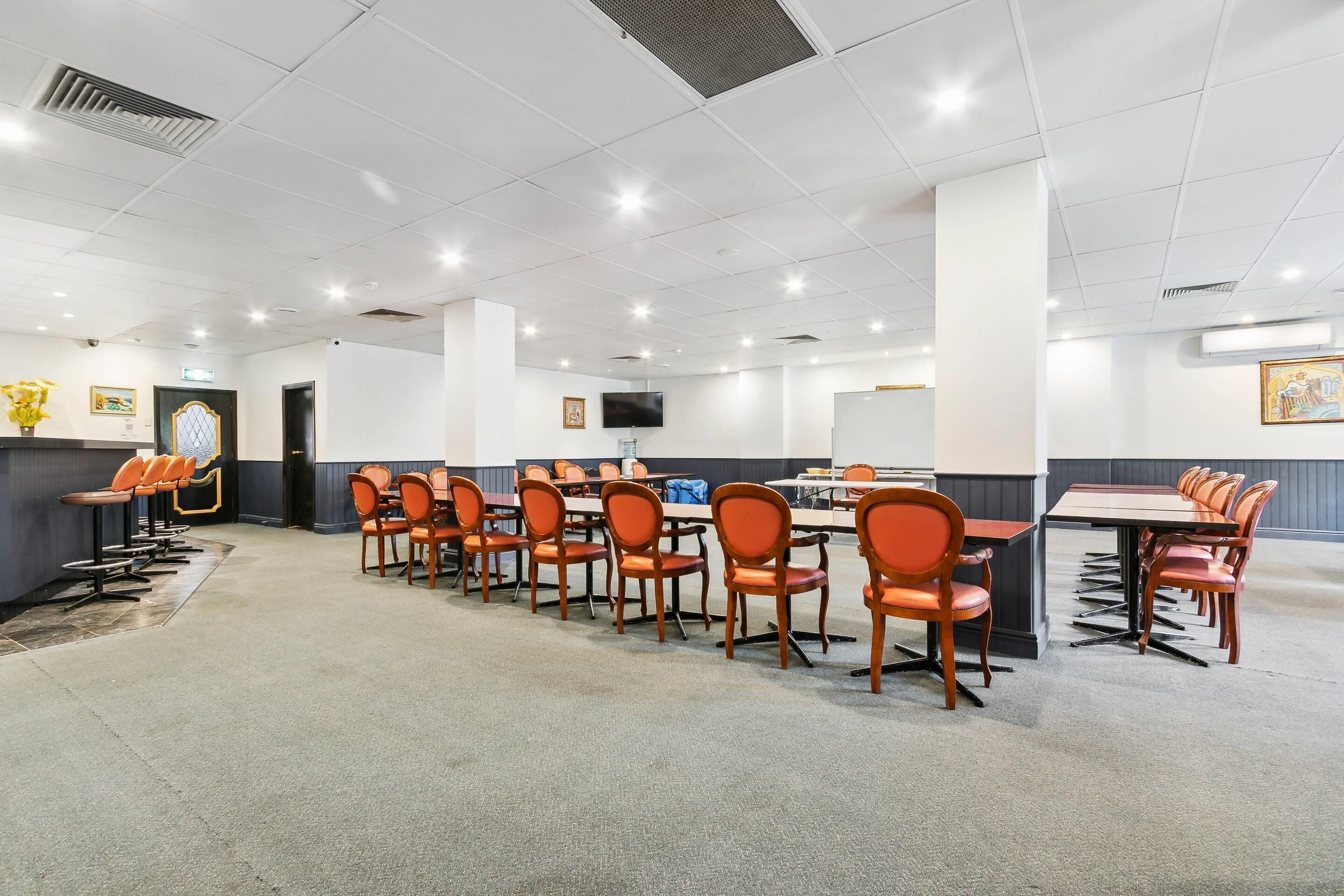 A conference room with rows of orange chairs and tables, a flat-screen TV, and a reception area with a counter and chairs.