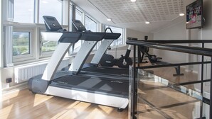 Een sportschool met loopbanden, trainingsapparatuur en grote ramen met uitzicht op het omliggende landschap.