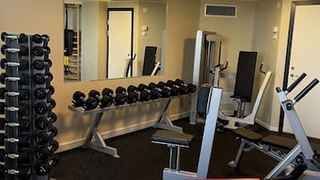 Un gimnasio con diverso equipamiento, incluyendo mancuernas, bancos y máquinas de pesas.