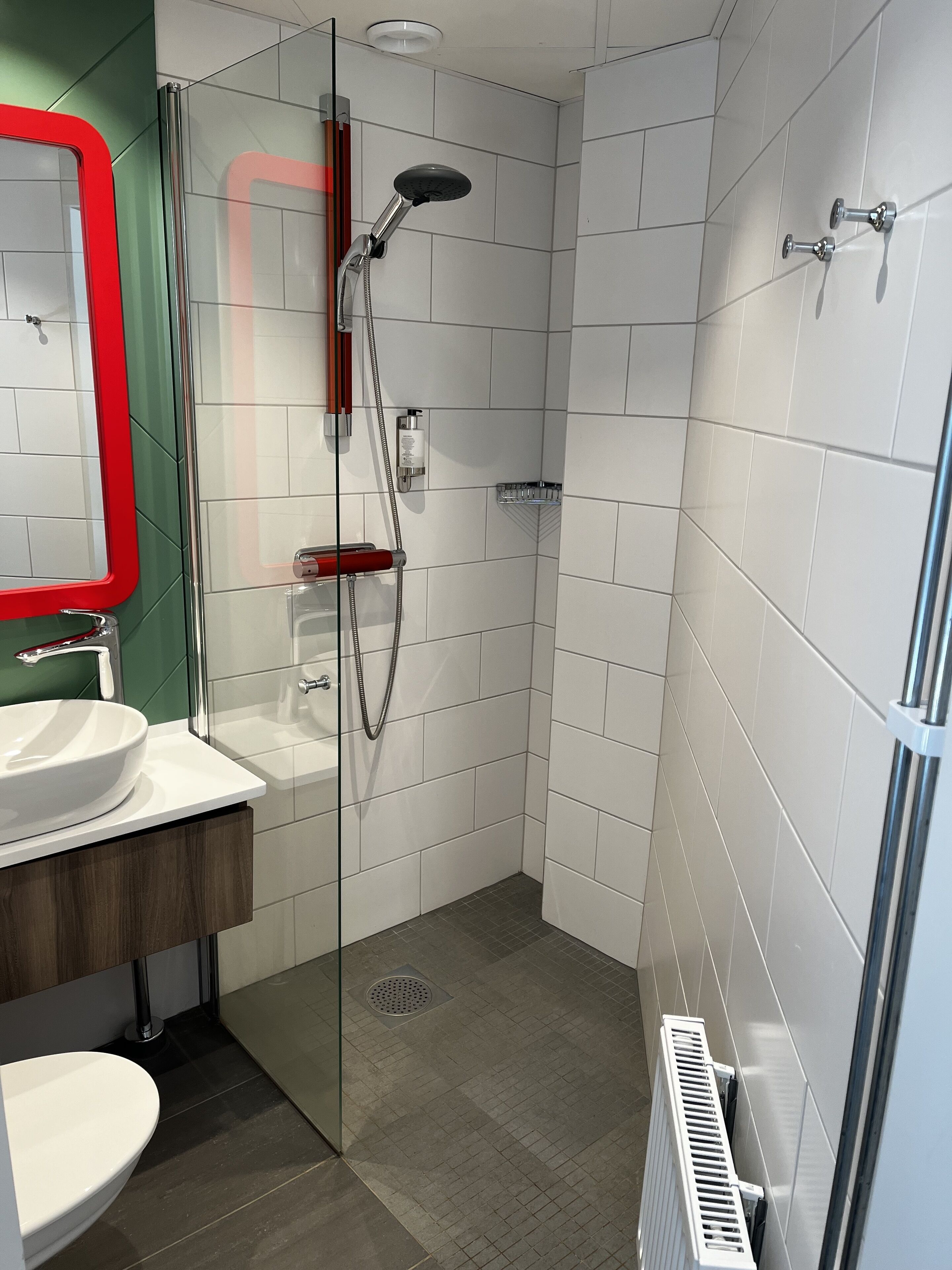 Een moderne badkamer met een douchecabine van glas, een wit wastafeltje en een spiegel met rode lijst.