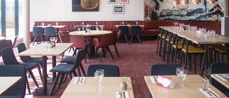 A restaurant with round tables, red booths, and a mural on the wall.