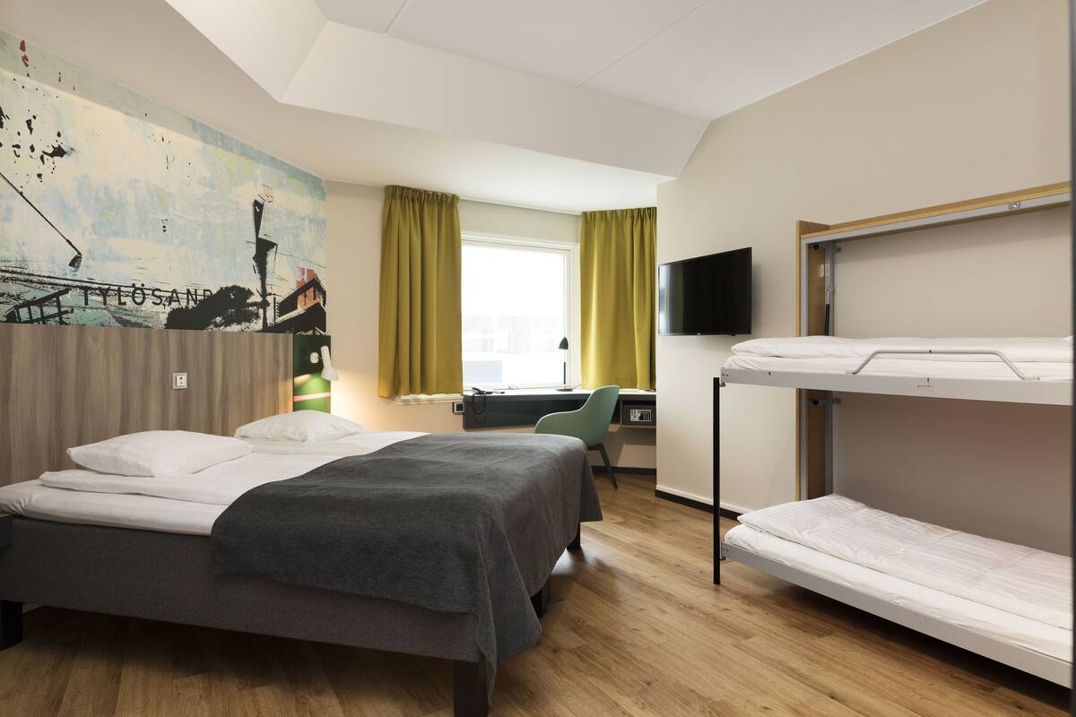 Habitación de hotel con dos camas individuales, un escritorio con silla, televisión y un mural en la pared.