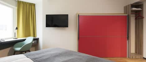 Habitación de hotel con cama, escritorio con silla, televisor y un armario rojo.