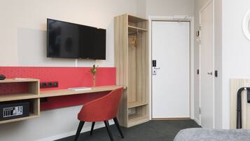 Una habitación de hotel con escritorio, televisión, armario y cama.