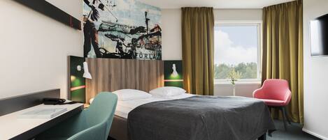 Una habitación de hotel con cama, escritorio, silla, obra de arte en la pared y ventana con cortinas.