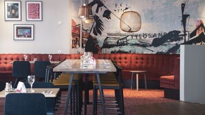 Een restaurant met een lange tafel gedekt voor diner, een rode, met kussens beklede bank, en een muurschildering.