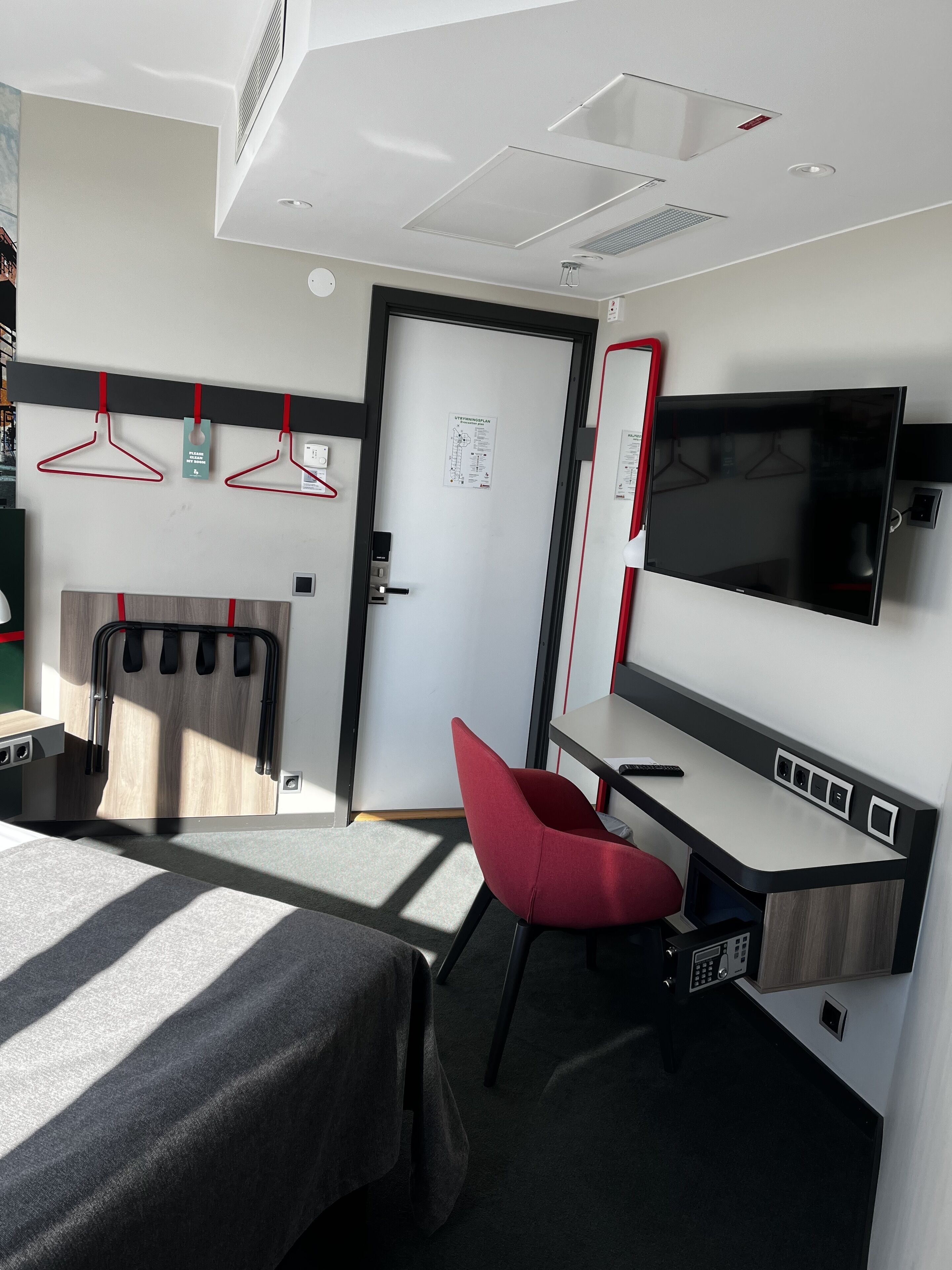 Una habitación de hotel moderna con una cama, un escritorio, una silla, un televisor y un armario.