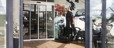 A hotel entrance with a glass door, a black chair, and a mural of a person climbing a mountain.