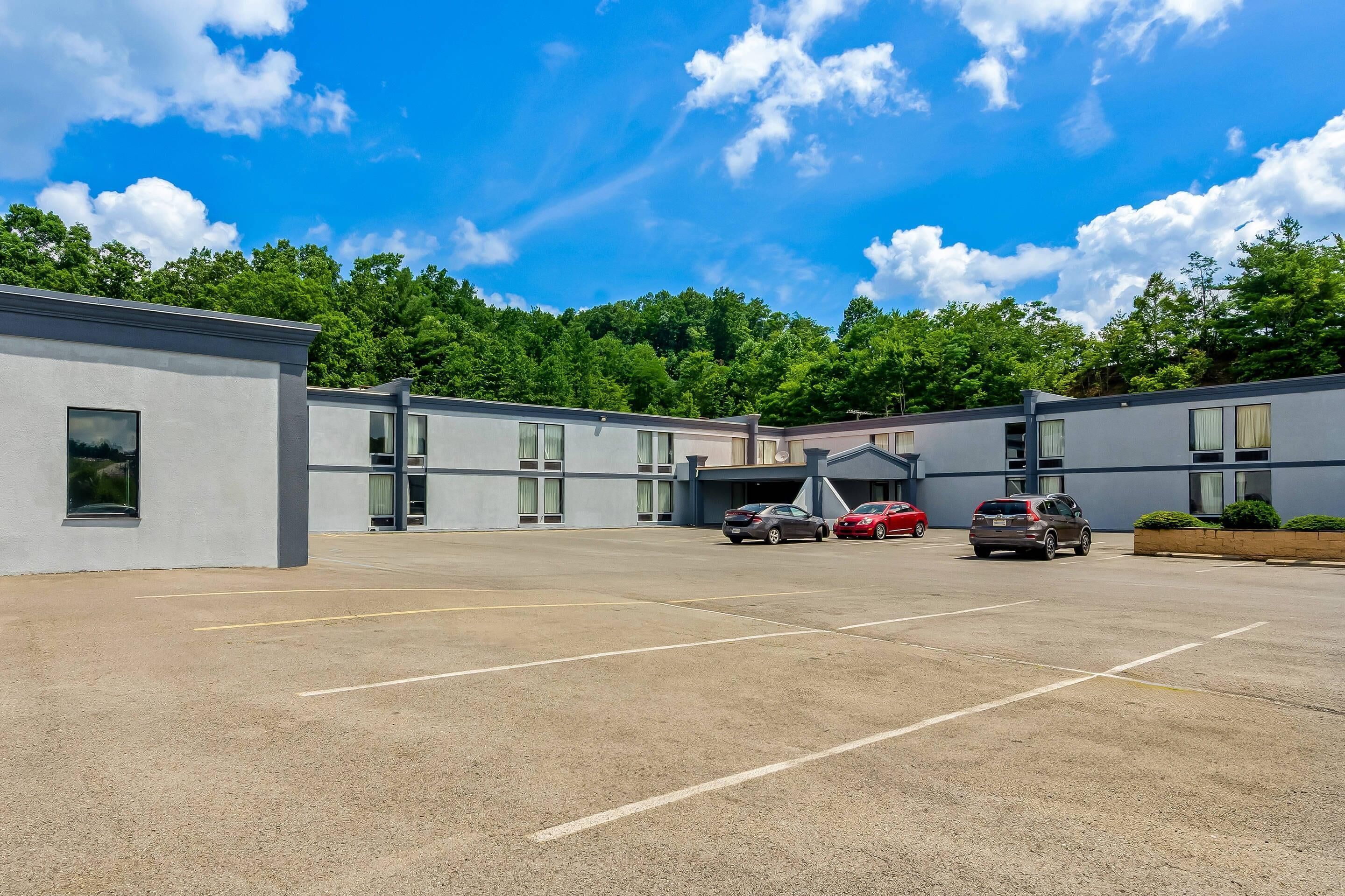 A parking lot with several cars, a building with large windows, and a forested background.