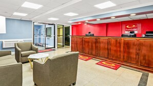 A reception area with a red wall, a wooden reception desk, and a seating area with sofas and a small table. - Econo Lodge Mt Hope - Beckley North (Mount Hope)