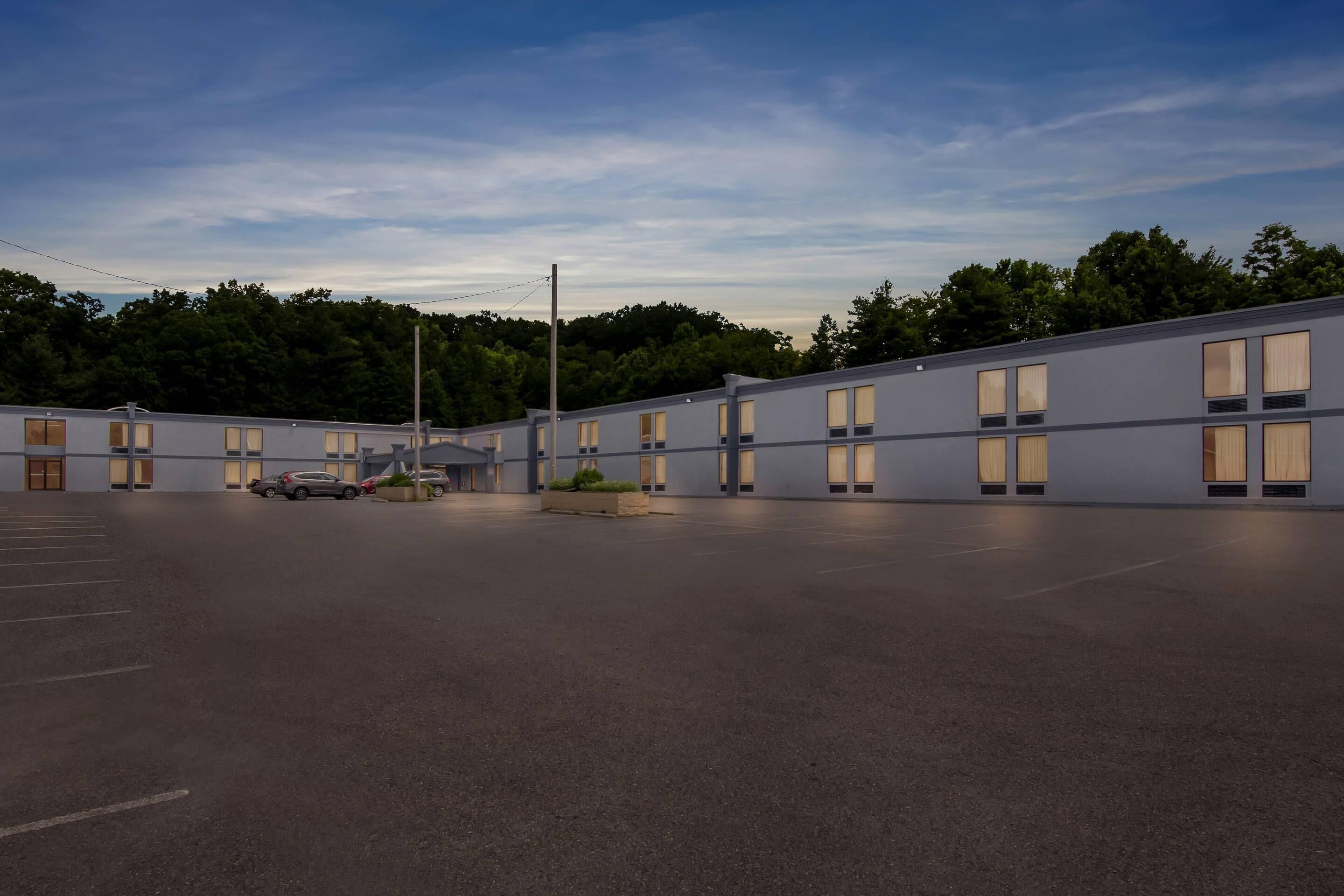 A modern motel with a parking lot, multiple rooms with large windows, and a landscaped area with plants.