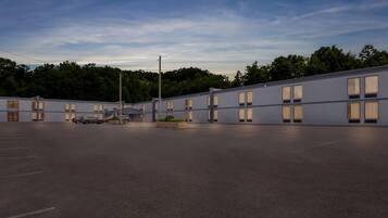 A modern motel with a parking lot, multiple rooms with large windows, and a landscaped area with plants.