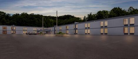 A modern motel with a parking lot, multiple rooms with large windows, and a landscaped area with plants.