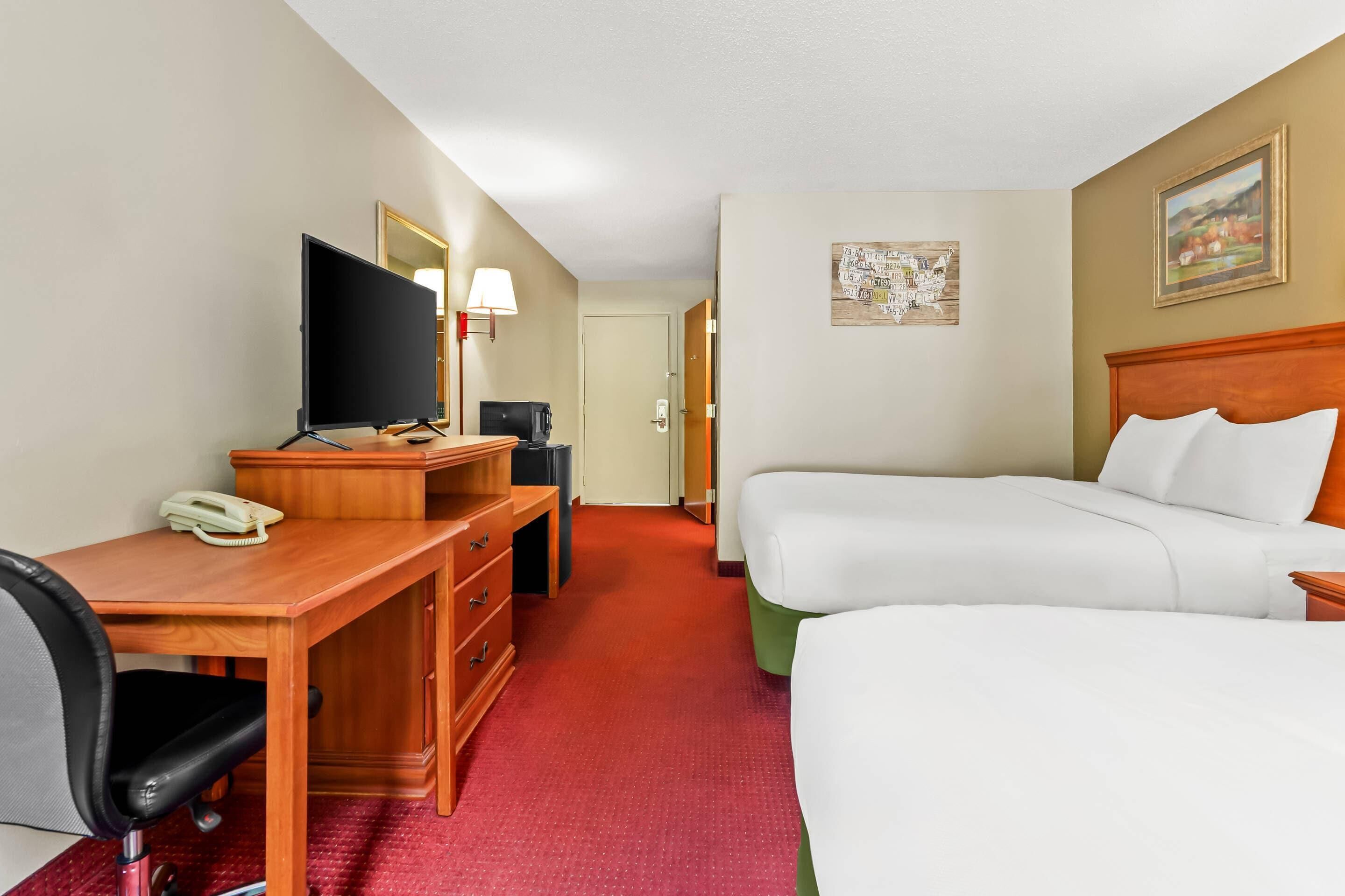 A hotel room with a desk, a television, a bed, and a door leading to another room.