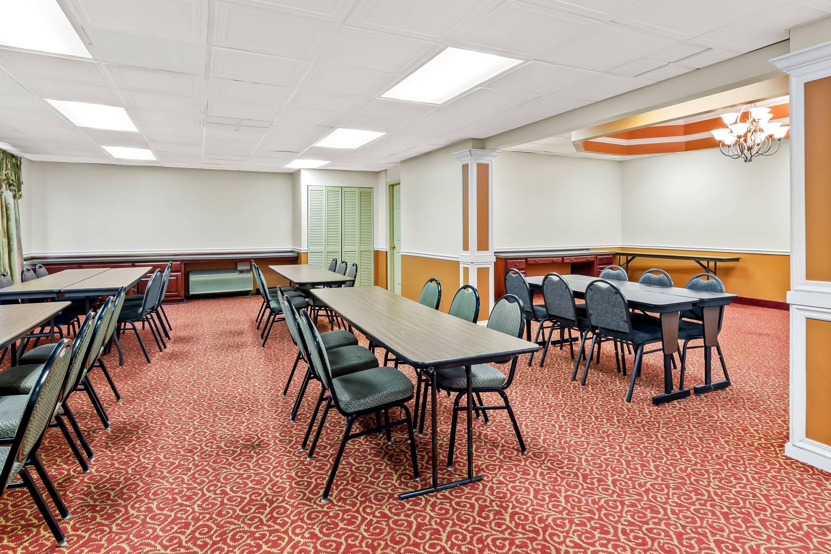 A conference room with multiple tables and chairs, carpeted floor, and a chandelier.