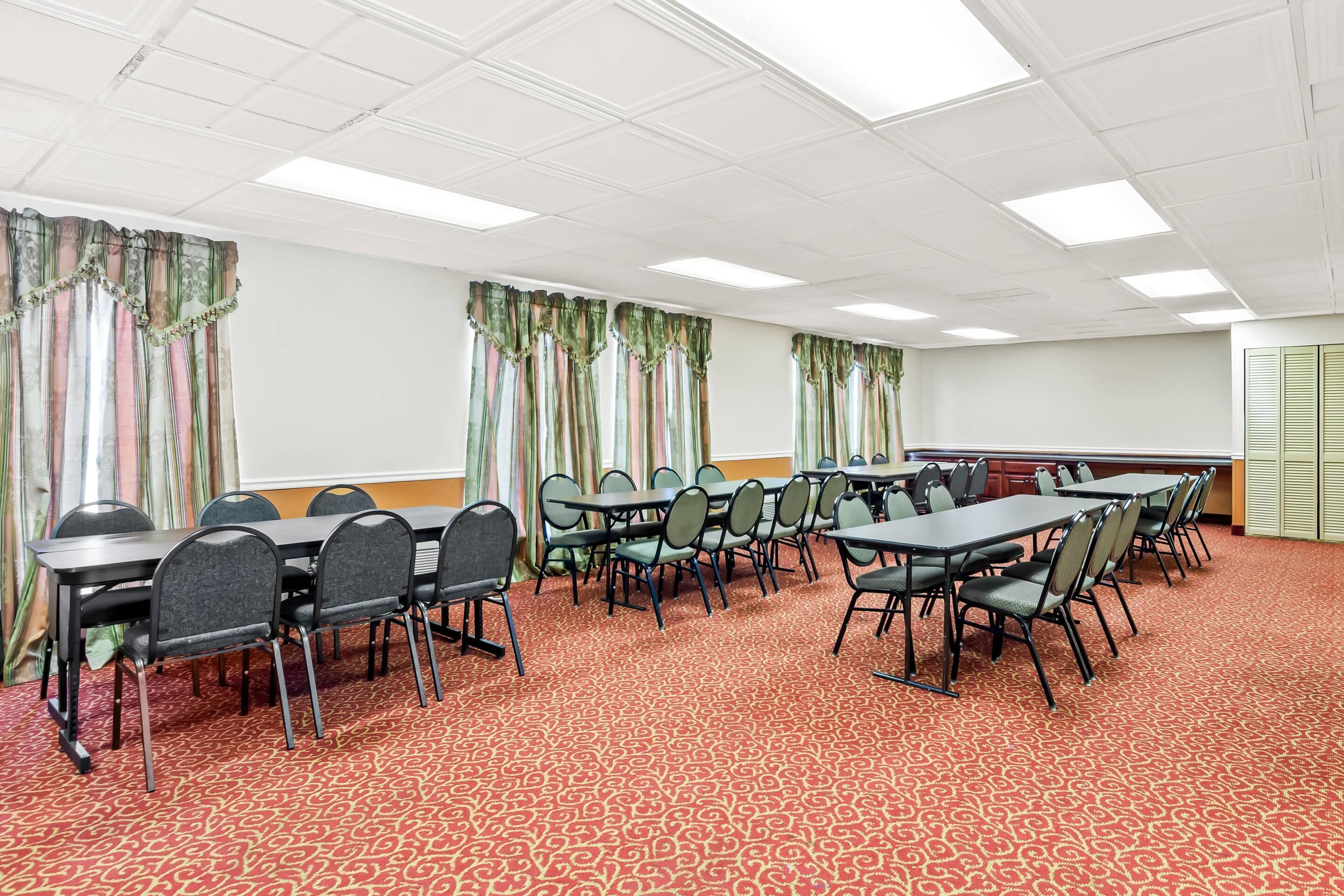 Una sala de conferencias con varias mesas y sillas, una alfombra estampada y cortinas.