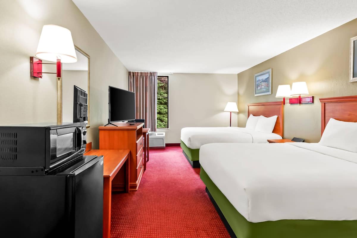 Ein Hotelzimmer mit zwei Betten, einem Fernseher, einem Schreibtisch mit Computer und einem roten Teppich.