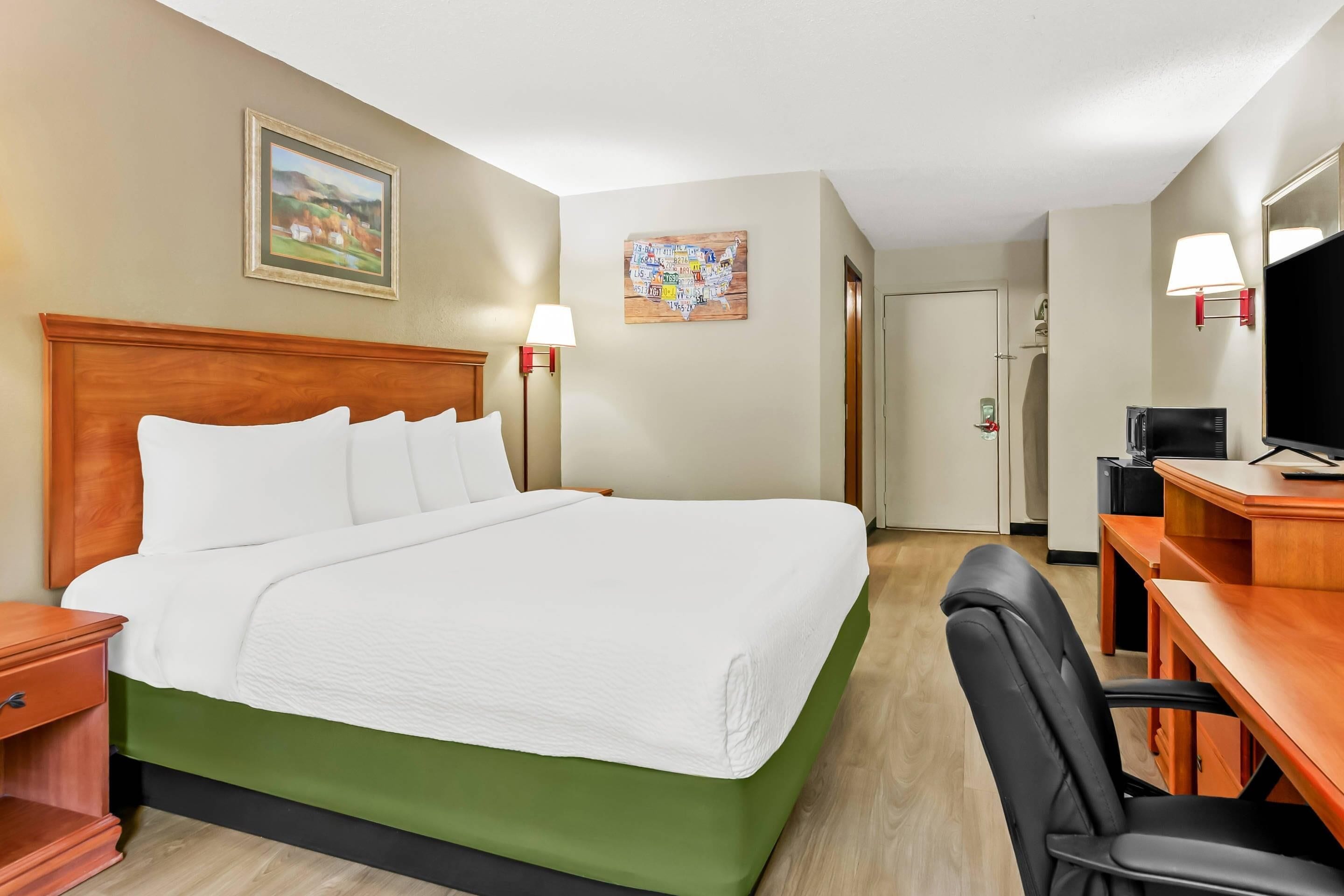 Une chambre d’hôtel avec un grand lit, un bureau avec une chaise, une télévision et un tableau au mur.