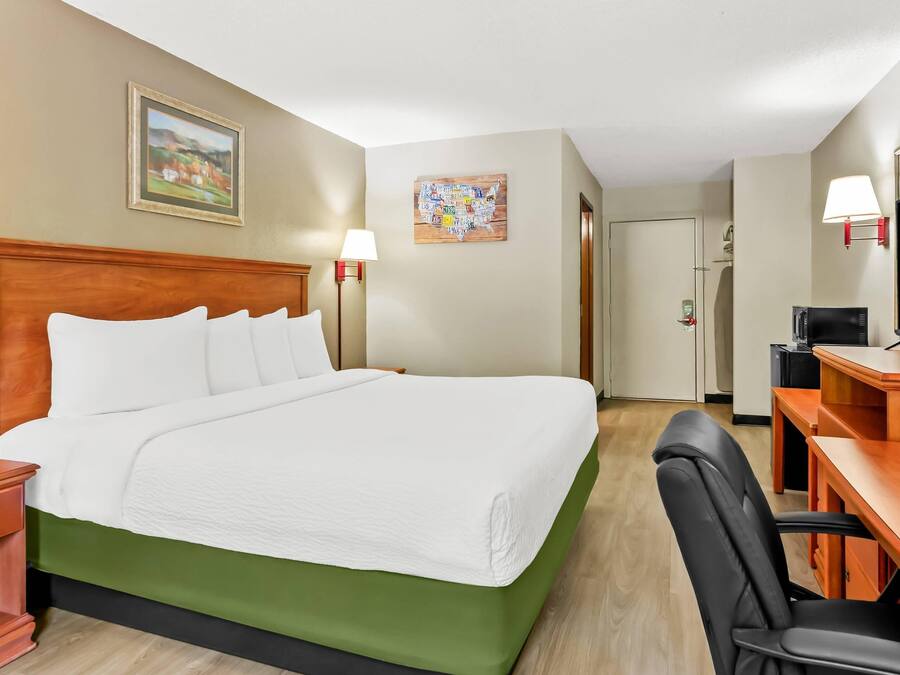 Une chambre d’hôtel avec un grand lit, un bureau avec une chaise, une télévision et un tableau au mur.