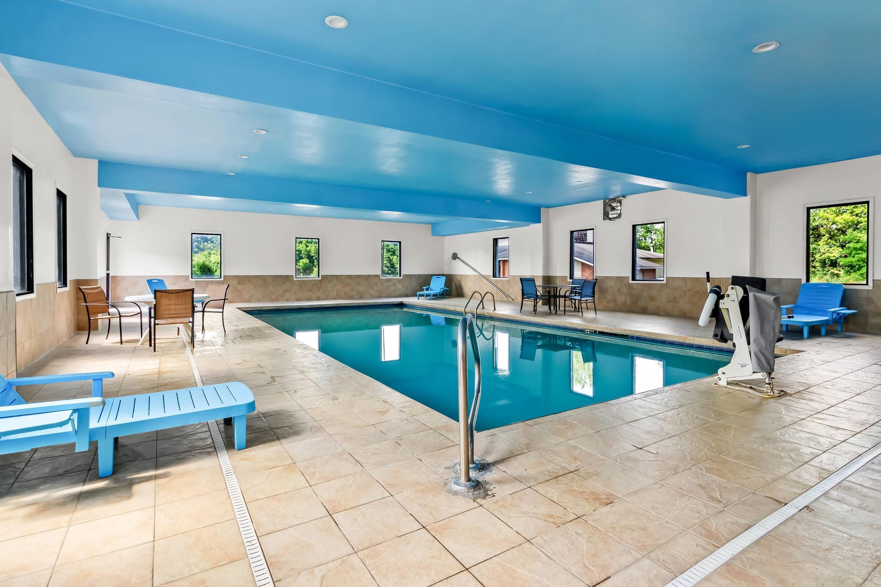 An indoor swimming pool with blue benches, a lifeguard stand, and a tiled floor.
