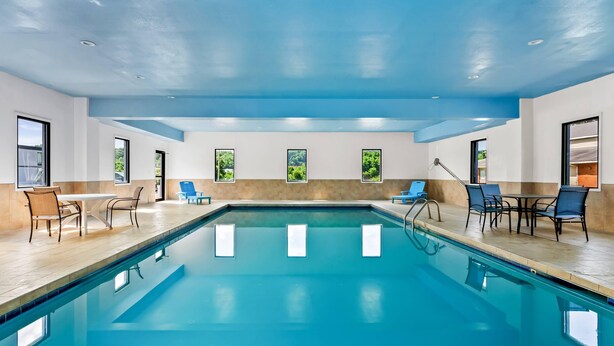 An indoor swimming pool with clear blue water, surrounded by lounge chairs and tables. - Econo Lodge Mt Hope - Beckley North (Mount Hope)