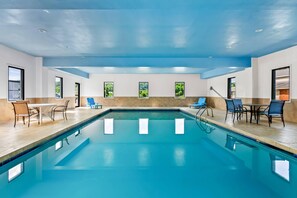 Una piscina interior con agua azul cristalina, rodeada de sillones y mesas.