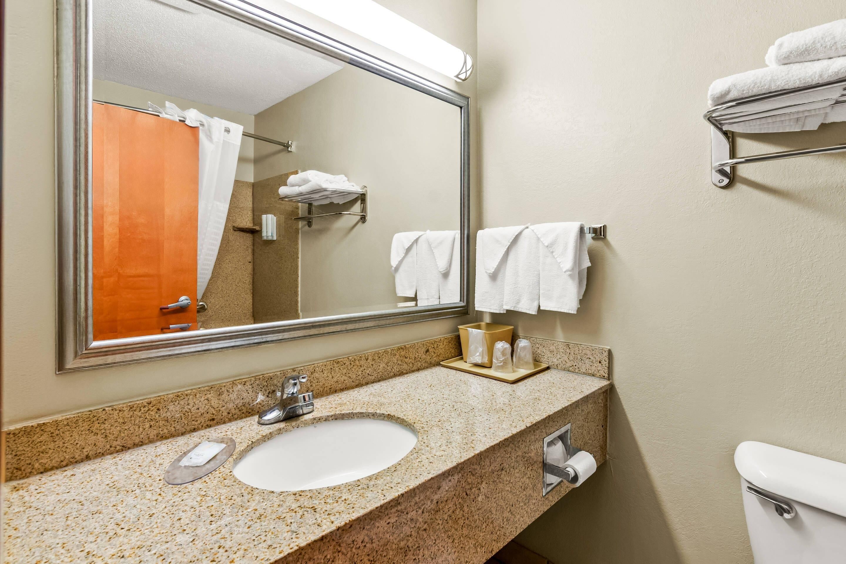 A bathroom with a granite countertop, a sink, a mirror, a towel rack, and a toilet.