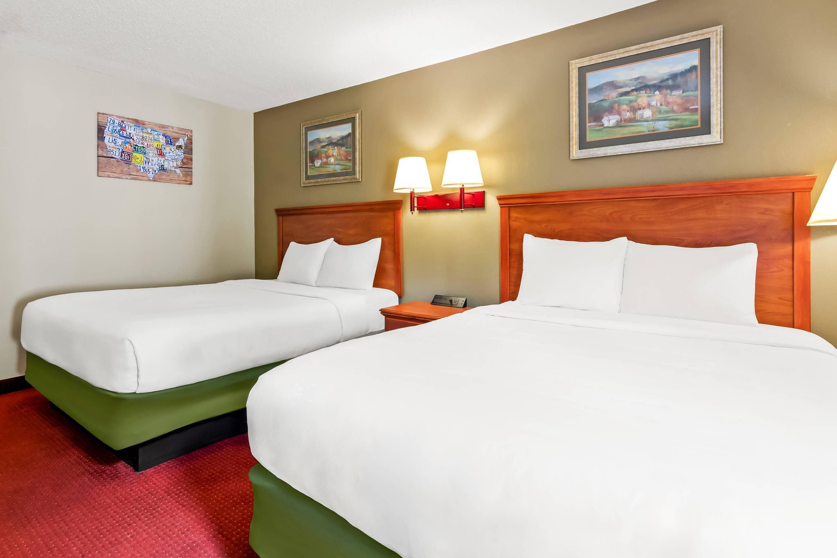 Una habitación de hotel con dos camas, una alfombra roja y dos lámparas de pared.