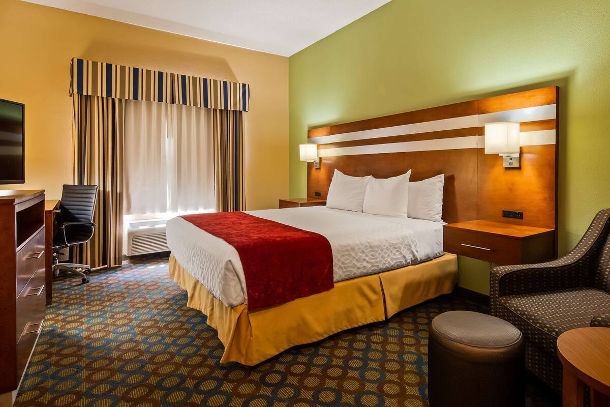 A hotel room with a bed, a desk, a chair, and a small table.