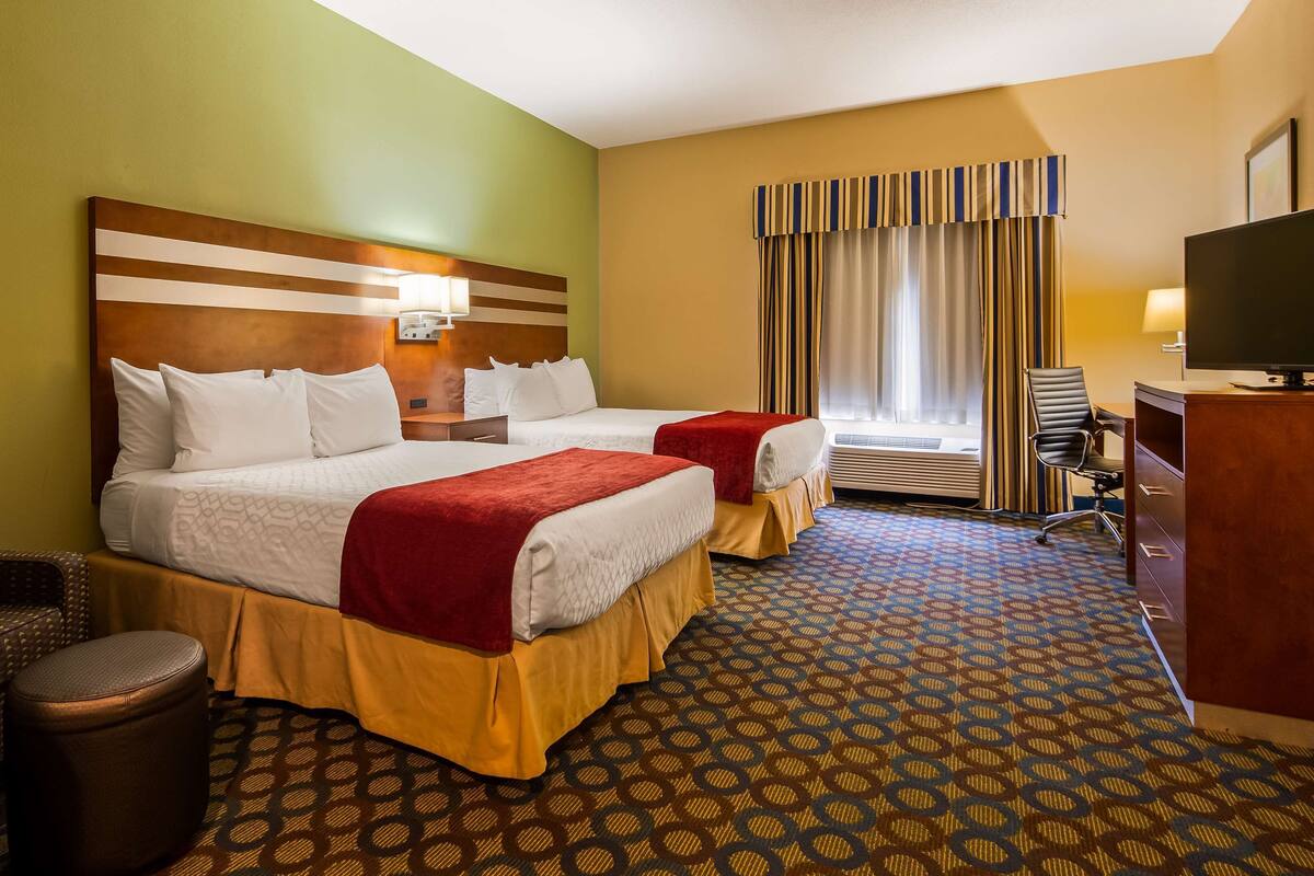 A hotel room with two beds, a desk, a chair, a TV, and a window with curtains.