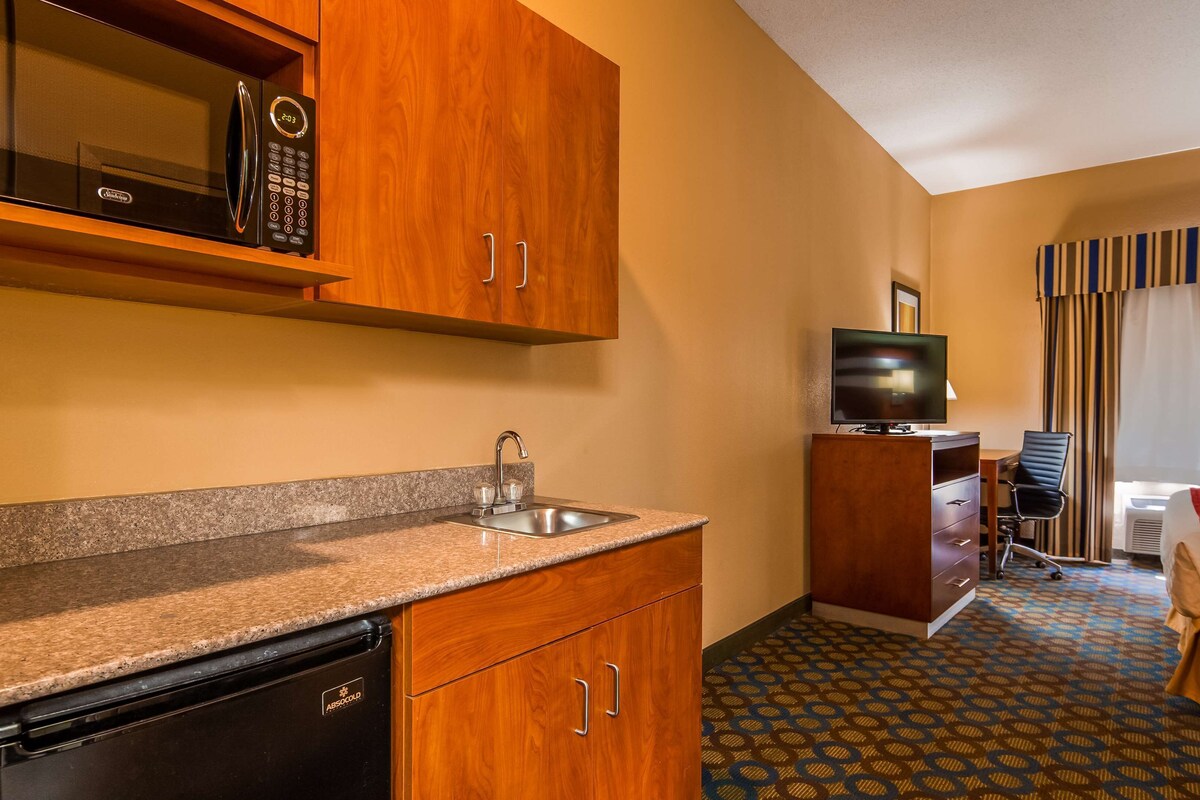 A compact hotel room with a kitchenette, a TV, a desk, and a chair.