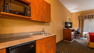 A compact hotel room with a kitchenette, a TV, a desk, and a chair.