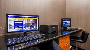 A hotel room with a Samsung monitor displaying a hotel booking site, a smaller monitor, a keyboard, a mouse, and a printer. - Best Western Troy Hotel (Troy)