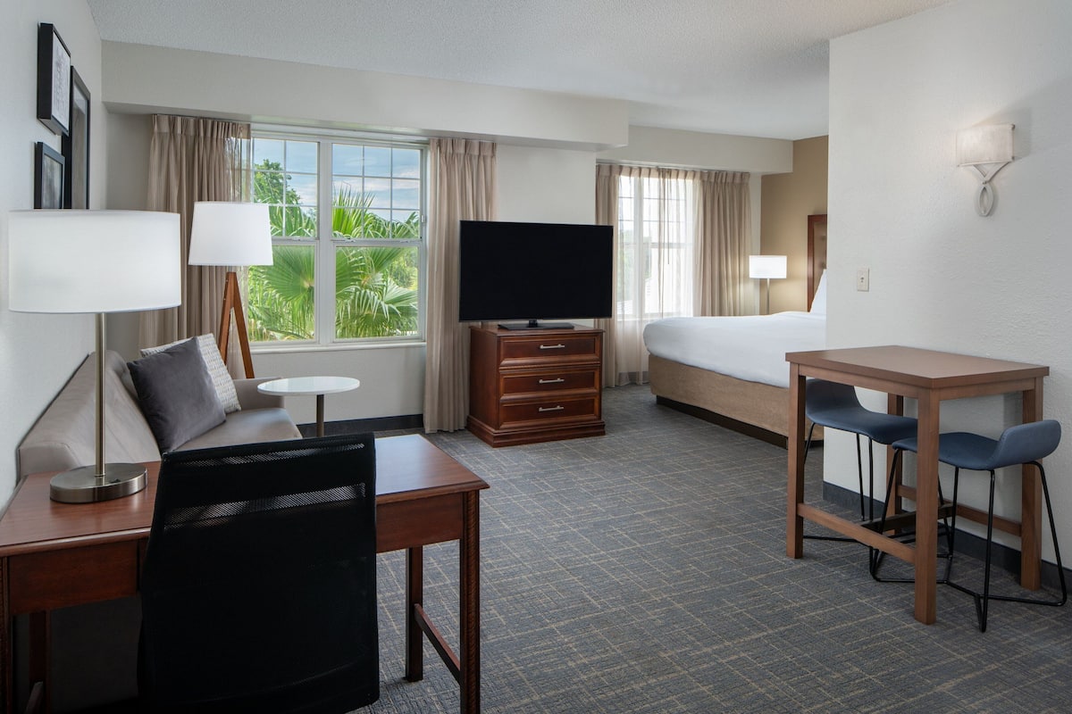 Ein Hotelzimmer mit Bett, Schreibtisch, Stuhl, Fernseher und Blick auf Grün durch das Fenster.