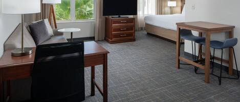 Une chambre d’hôtel équipée d’un lit, d’un bureau, d’une chaise, d’une télévision et offrant une vue sur la verdure par la fenêtre.
