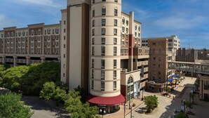 A multi-story hotel with a distinctive cylindrical tower, a covered entrance, and a parking garage in the background.