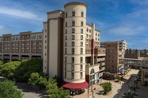 A multi-story hotel with a distinctive cylindrical tower, a covered entrance, and a parking garage in the background.