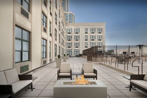 A rooftop terrace with outdoor seating, a fire pit, and a view of a tall building.