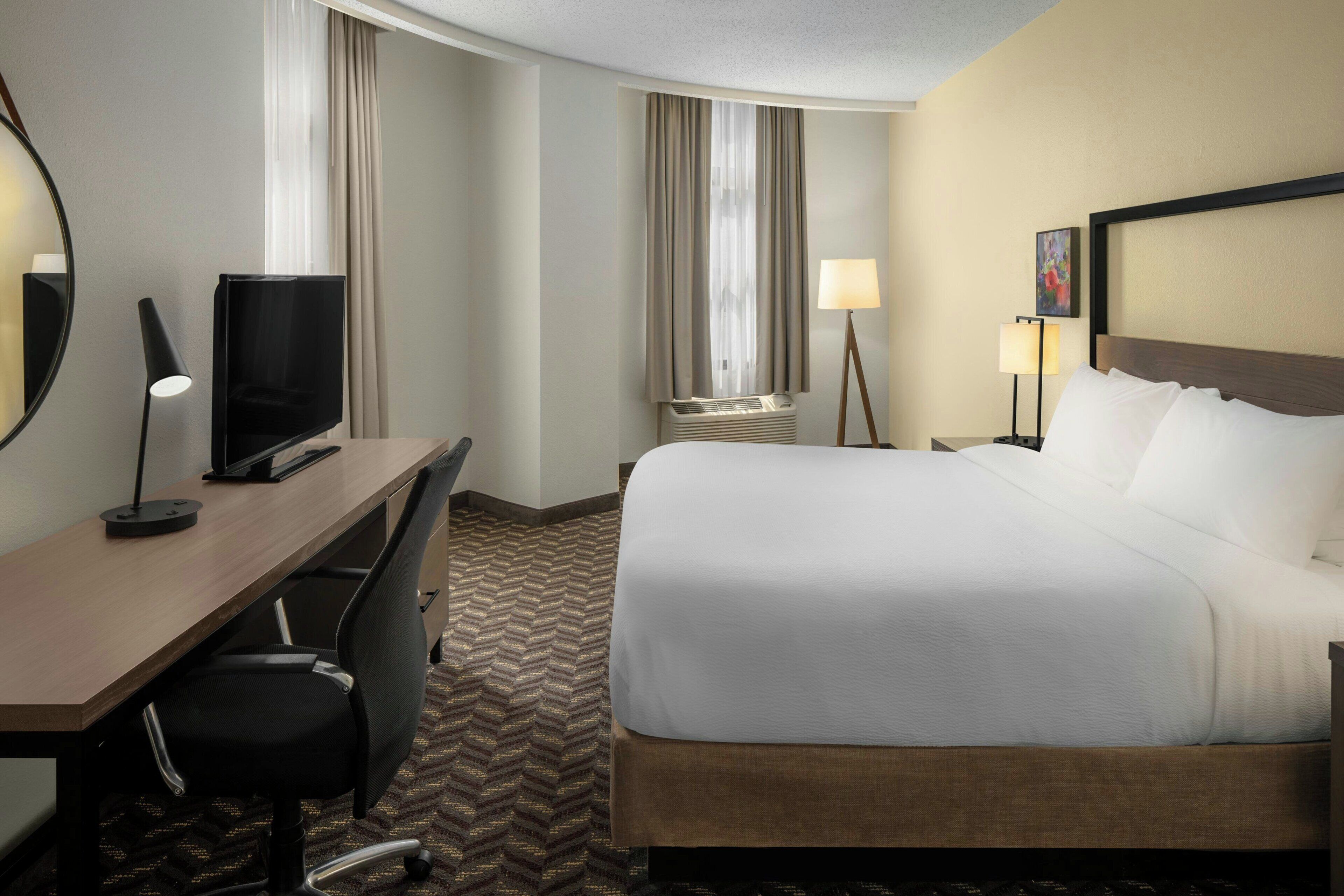 A hotel room with a bed, desk, chair, television, and lamps.