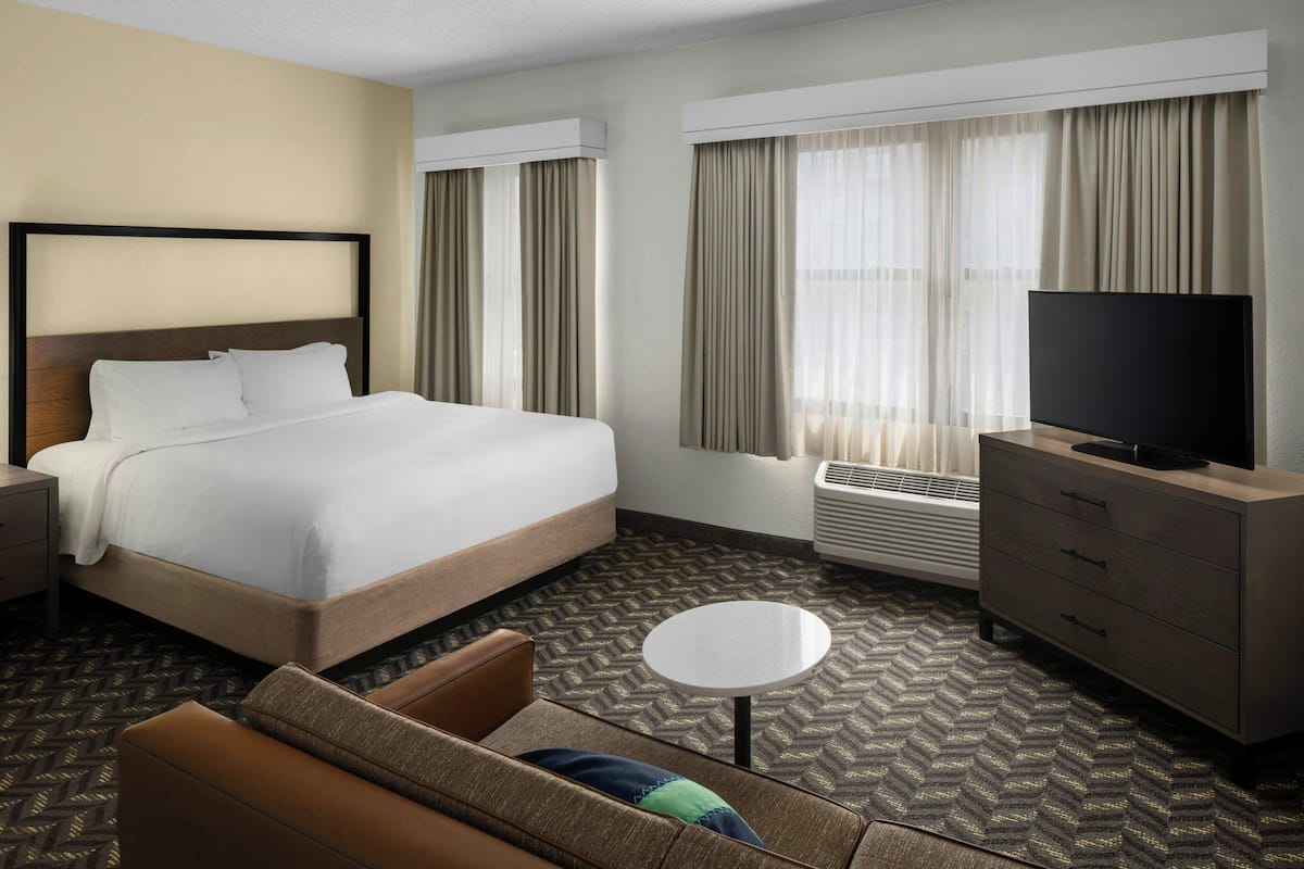 A hotel room with a large bed, a TV, a sofa, a small table, and a heater.