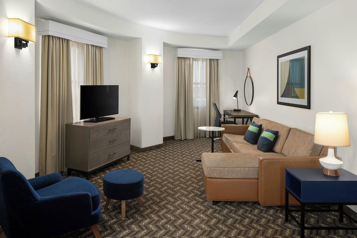 A hotel room with a TV, a sofa, a desk, and a lamp.