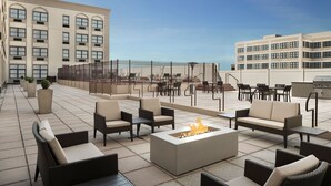 A rooftop patio with outdoor seating, a fire pit, and a view of the cityscape.