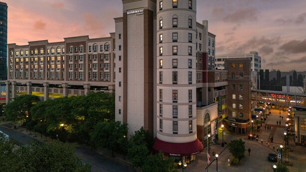 A multi-story hotel with a distinctive cylindrical tower, a red awning, and a row of windows.