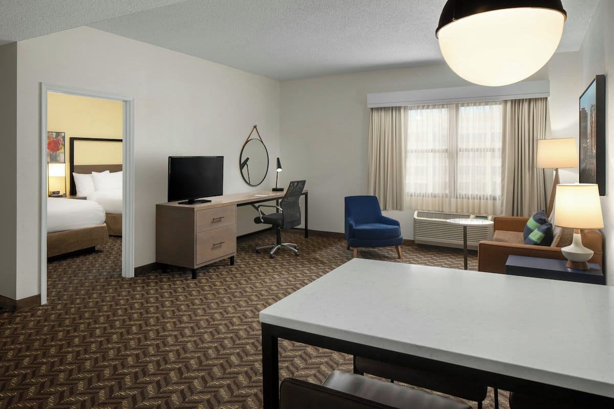 A hotel room with a bed, desk, chair, TV, and a large window with curtains.