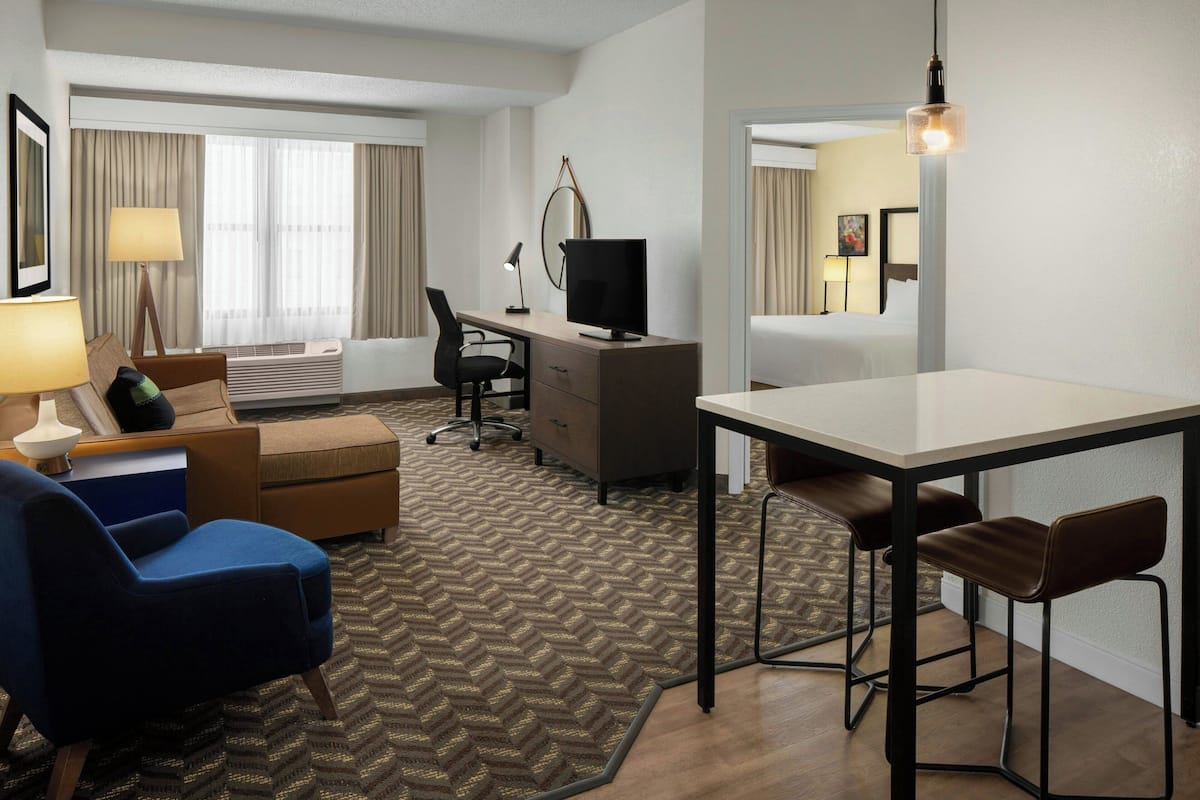 A hotel room with a desk, computer, two chairs, a sofa, a lamp, and a bed.