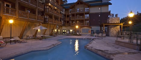 Zona de piscina con sillas de descanso y sombrillas, rodeada de edificios de varios pisos con balcones.