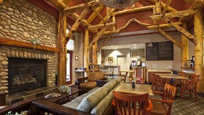 Un intérieur rustique agrémenté d’une cheminée en pierre, de poutres en bois, d’un long banc et d’un coin repas avec des chaises et des tables en bois.
