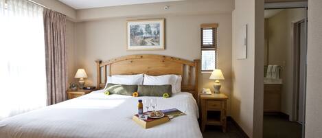 A hotel room with a large bed, two bedside tables with lamps, a framed picture on the wall, and a door leading to a bathroom.