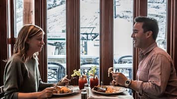 A couple dining at a table with a view of a snowy mountain and ski lift in the background.